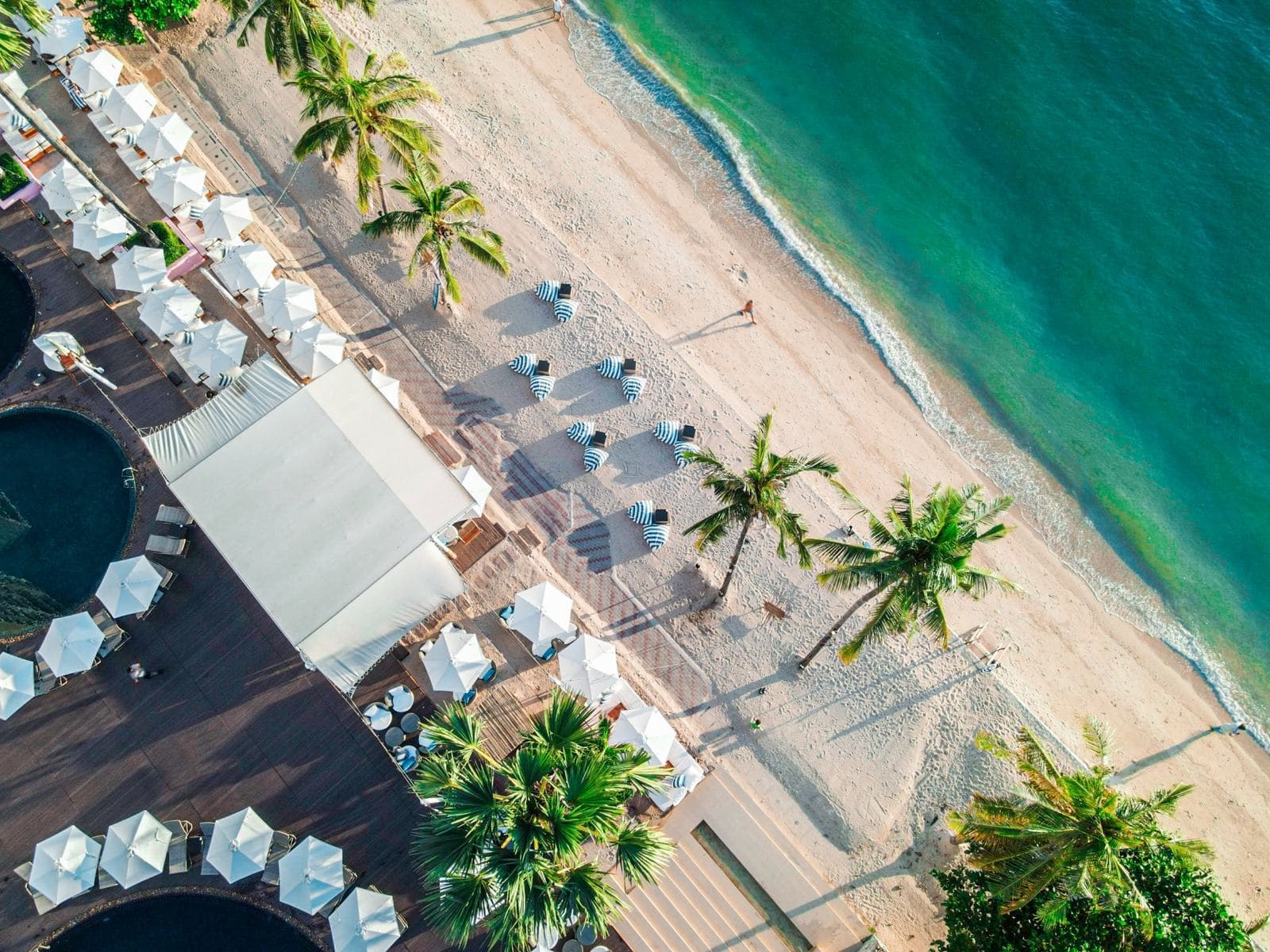 Вид сверху на пляж отеля Pullman Pattaya Hotel G: ряды белых зонтов у бассейнов, пальмы и бирюзовая вода залива
