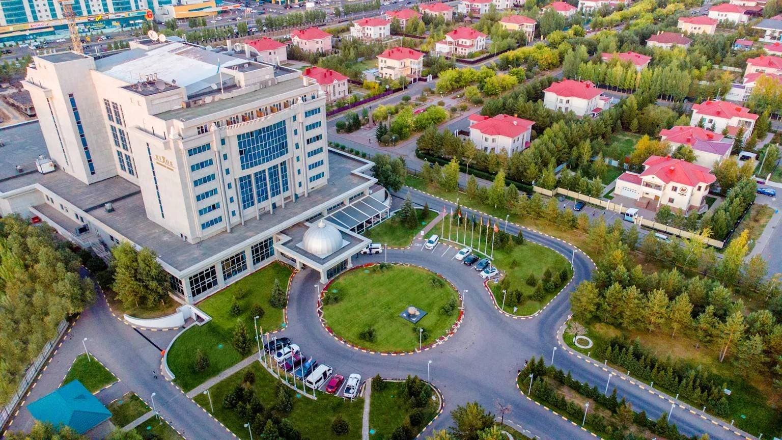 Отель Rixos President Astana с высоты: здание с куполом над входом, круговой подъезд, рядом зелёный квартал с красными крышами