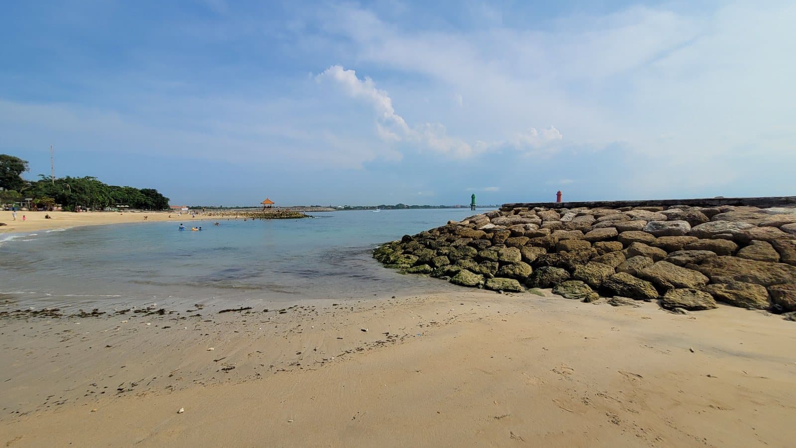 Песчаный пляж Санура, каменный волнорез и спокойная вода под голубым небом